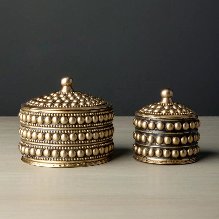Two decorative brass containers with intricate designs on a neutral background