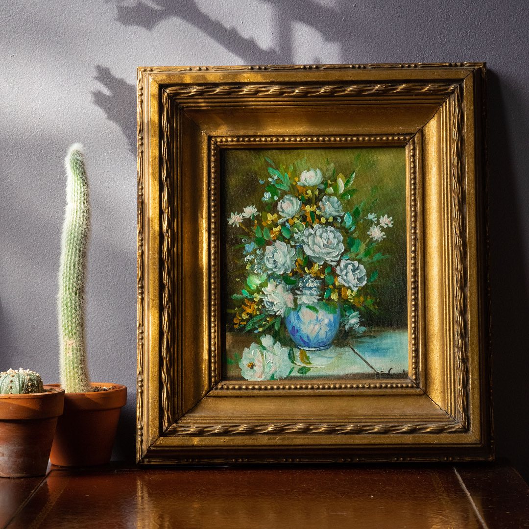 Framed painting of flowers on a table with cacti in the background