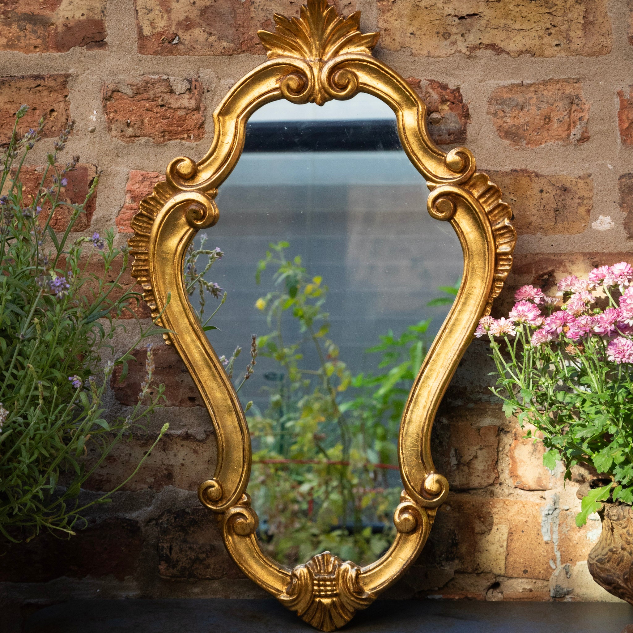 Decorative gold mirror on a brick wall with plants