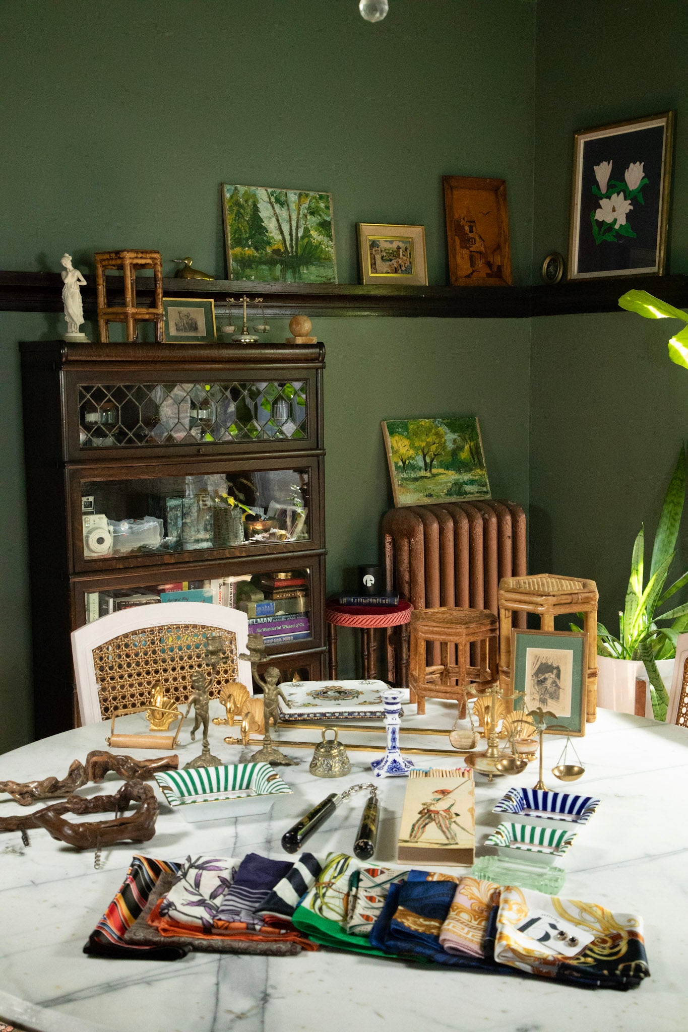 Room with a table displaying various decorative items, including a bookshelf and wall art.