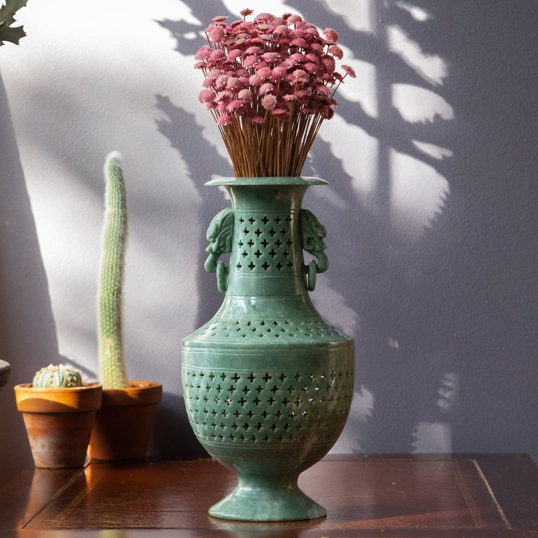 Decorative green vase with pink dried flowers on a wooden surface