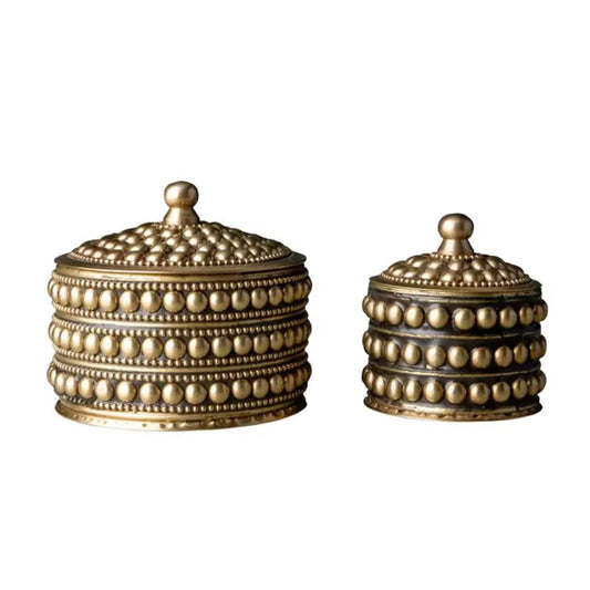 Two decorative brass containers with intricate designs on a white background