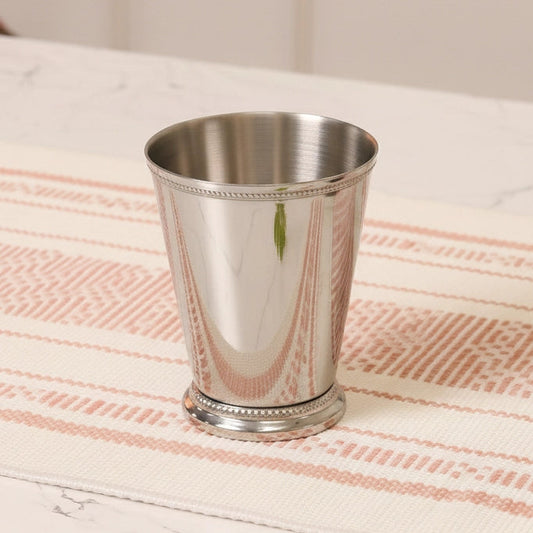 Silver mint julep cup on a striped tablecloth with mint leaves.