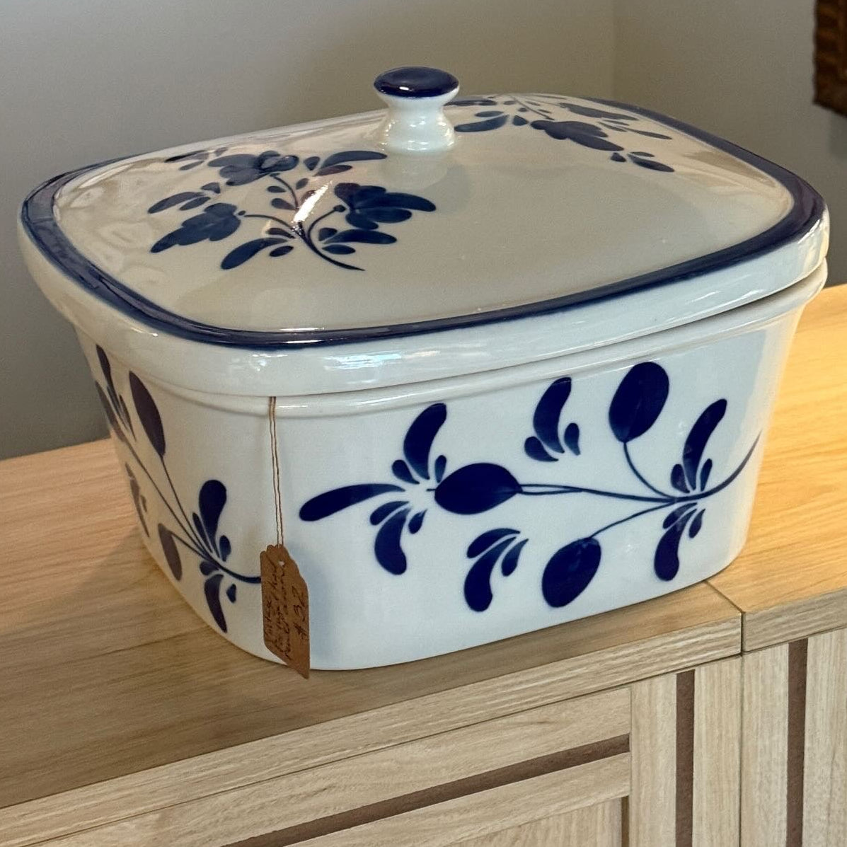 A vintage Portuguese hand-painted dish with a lid, featuring a white glaze and dark blue floral patterns, displayed on a wooden cabinet with a text overlay describing it as '$32'.