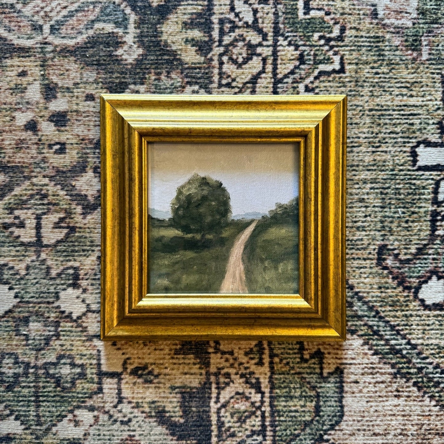Small painting of a landscape with a gold frame on a textured wall.