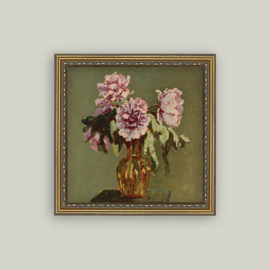 A framed still life painting featuring pink flowers in a vase against an olive-green background, enclosed in a decorative gold-toned frame and shown on a light gray wall.