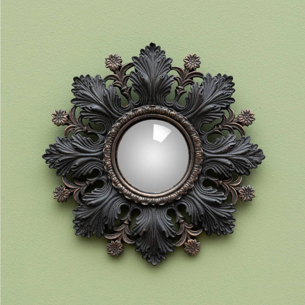 An ornate round wall mirror with a dark, decorative acanthus leaf frame, mounted on a solid sage green wall.