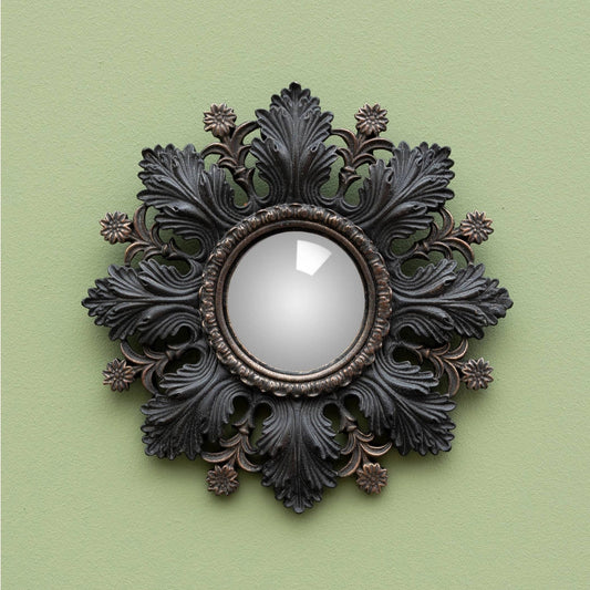 An ornate round wall mirror with a dark, decorative acanthus leaf frame, mounted on a solid sage green wall.