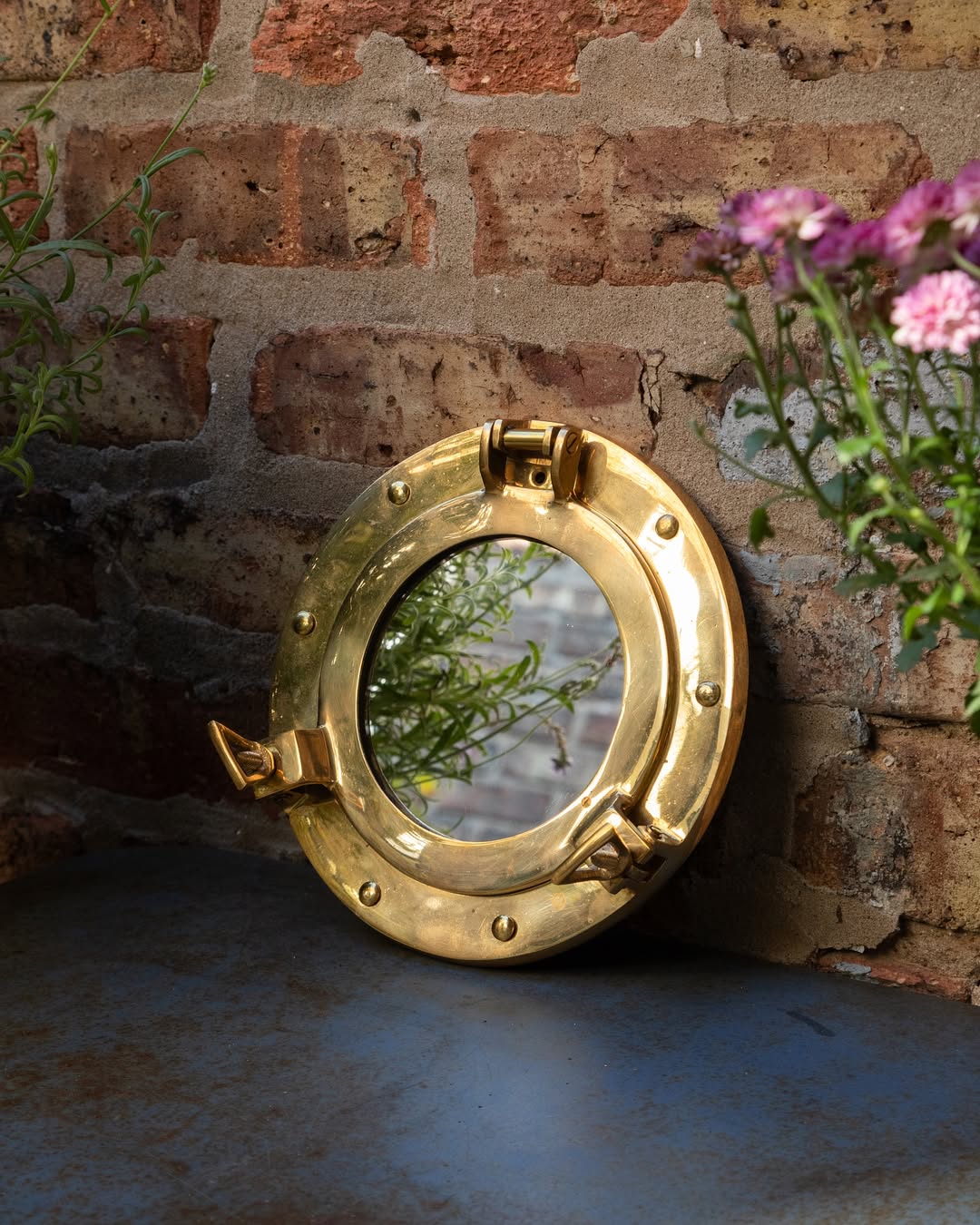 Gold porthole mirror on a brick wall with flowers