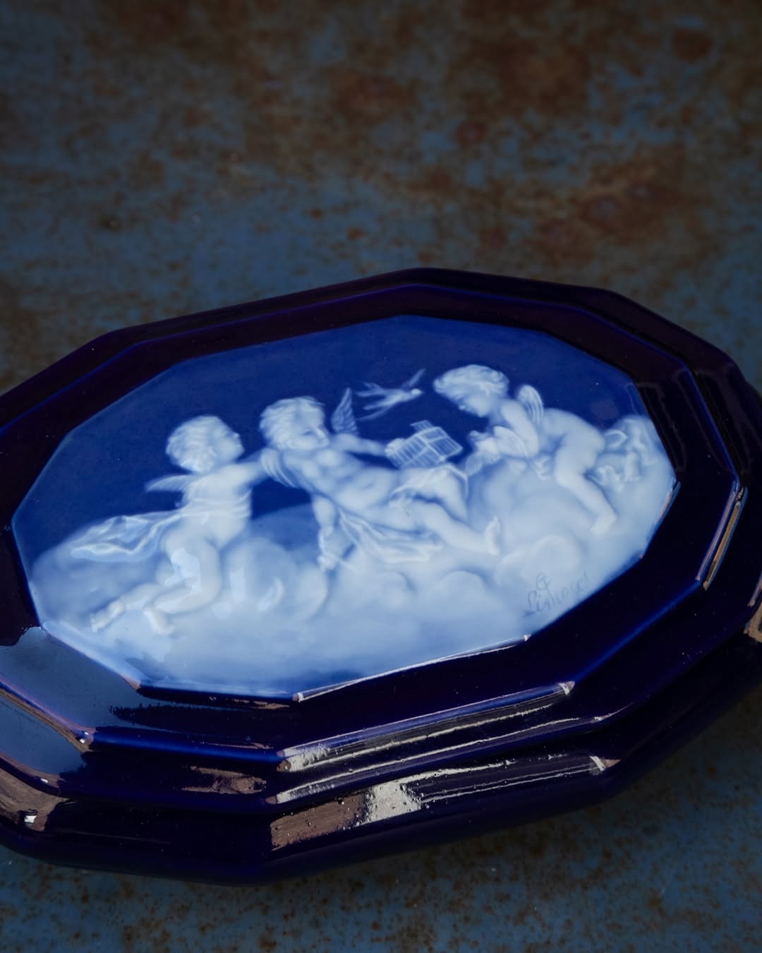 Decorative trinket box with a blue and white cherub design on a textured surface