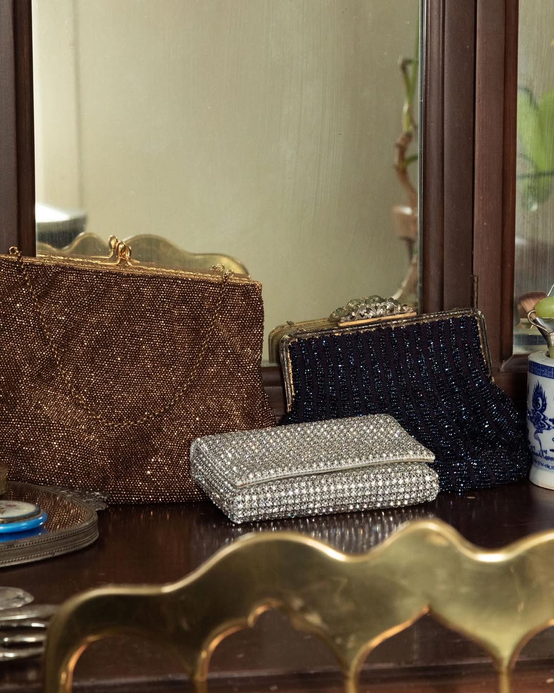 Three glittery handbags on a reflective surface with a mirror in the background
